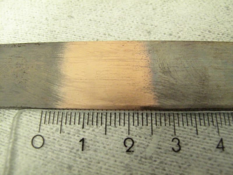 Stark oxidiertes und verschmutztes Bandmaterial, bestehend aus einer technischen CuAg Legierung. Im mittleren Bereich ist der Effekt einer reduzierenden Plasmabehandlung zu sehen.